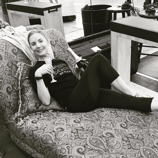 Clare poses on a chaise lounge with a champagne flute and bottle